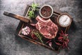 Raw beef steak on wooden cutting board with salt spices chili peppers thyme and rosemary