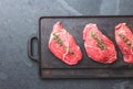 Raw beef steaks with herbs and spices on cast iron frying board, top view Royalty Free Stock Photo