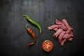 Raw beef strips, half ripe tomato and two hot pepper pods on black