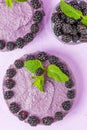 Raw blackberry dessert decorated with fresh ripe forest berries and green mint leaves on pastel violet background.