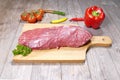 Raw Braten meat on a wooden cutting board with peppers and tomatoes on the side