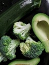 Raw broccoli, zucchini and half a pitted avocado on the black background. Only green vegetables. Healthy vegan eating. Royalty Free Stock Photo