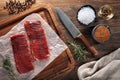 Raw calf flank beef on white cooking paper and wooden cutting table. Decorated with herbs, spices and knife