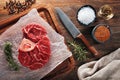 Raw calf shank beef with bone on white cooking paper and wooden cutting table. Decorated with herbs, spices and chef`s knife