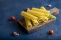 Raw cannelloni pasta on cutting board on blue background with cherry tomatoes, garlic and basil. Royalty Free Stock Photo