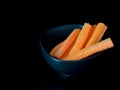 Raw carrot stick in dark bowl on black with copy space