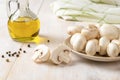 Raw champignons on a plate and olive oil jar on a white wooden table. Cooking fresh button mushrooms Agaricus bisporus. Concept of Royalty Free Stock Photo