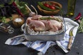 Raw chicken in a baking dish on a kitchen towel on a dark background.