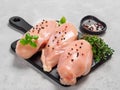 Raw chicken breast with fresh basil on black cuttingboard over cement background