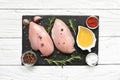 Raw chicken breasts witn rosemary, olive oil and spices on black slate cutting board