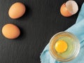 Raw chicken egg in a glass cup, dark stone background. Top view of a bright yolk, next to an egg shell, two whole eggs. The