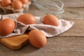 Raw chicken eggs, napkin, board and whisk on wooden table, closeup