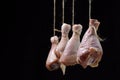 Raw chicken legs on a black background. Chicken legs hang suspended by a thread.