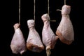 Raw chicken legs on a black background. Chicken legs hang suspended by a thread.