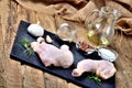 Raw chicken legs on a cutting board with a fresh rosemary, garlic, cumin, pepper and salt on a wooden table, jug with Royalty Free Stock Photo