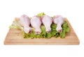 Raw chicken legs and lettuce leaf on wooden cutting board isolated on white background. Four fresh legs for cooking. Side view. Royalty Free Stock Photo