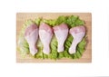 Raw chicken legs and lettuce leaf on wooden cutting board isolated on white background. Four fresh legs for cooking. Top view. Royalty Free Stock Photo