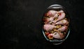 Raw chicken legs and lots of spice in a transparent dish on a black background. Royalty Free Stock Photo