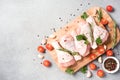 Raw chicken legs with seasonings and vegetables on wooden cutting board over light gray concrete background Royalty Free Stock Photo