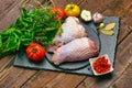 Raw chicken legs on a slate stone plate with spices, colorful tomatoes and red currant on a wooden rustic background