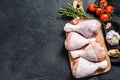 Raw chicken legs with spices and vegetables on a wooden cutting board. Black background. Top view. Copy space Royalty Free Stock Photo