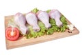 Raw chicken legs on wooden cutting board isolated on white background. Four legs with lettuce leaf, garlic, tomato and black peppe Royalty Free Stock Photo