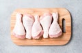 Raw chicken legs on wooden cutting board over gray concrete background. Chicken drumsticks ready to cook Royalty Free Stock Photo