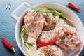 Raw chicken legs (drumsticks) in white baking dish, closeup. Black stone background, small chili pepper and rosemary