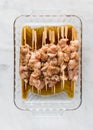 Raw chicken marinading on wooden bamboo skewers in a glass dish.