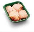 Raw chicken thighs in a green tray over white background