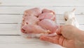 Raw chicken thighs in a plastic container in a woman's hands, and fresh garlic bulbs close-up on a white wooden background Royalty Free Stock Photo