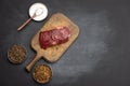 Raw classic beef steak on a brown wooden board, spice mix, salt on a black table Royalty Free Stock Photo