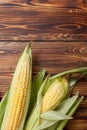 Raw cobs of young corn with leaves on a wooden table