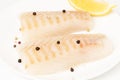 Raw cod fish pieces on the plate spiced with salt, peppercorns and lemon isolated on white background Royalty Free Stock Photo