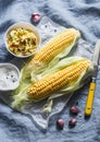 Raw corn cob and aromatic spicy butter on a blue background, top view.