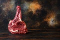 Raw Cowboy beef marbled steak in butchery side view over rustic old cutting board with dark planks. space for text Royalty Free Stock Photo