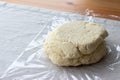 Raw curd dough with bits of cottage cheese on a plastic wrap on a linen tablecloth on a wooden table