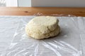 Raw curd dough with bits of cottage cheese on a plastic wrap on a linen tablecloth on a wooden table