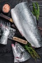 Raw cut salmon fish on a wooden cutting board with chef cleaver. Black Wooden background. Top view