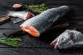 Raw cut salmon fish on a wooden cutting board with chef cleaver. Black Wooden background. Top view