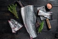 Raw cut salmon fish on a wooden cutting board with chef cleaver. Black Wooden background. Top view