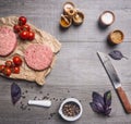 Raw cutlet for burgers, with cherry tomatoes and herbs on a packaging paper with unground black pepper, knife meat on wooden r