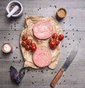 Raw cutlet for burgers, with cherry tomatoes and herbs on a packaging paper with unground black pepper, knife meat on wooden r