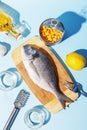 Raw dorado fish on a wooden board, ingredients for cooking and spices on a blue background