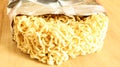 Raw dried instant noodles on a round wooden cutting board in an unnamed foil packaging with no name close up on a yellow