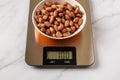 Raw dried peanut in a bowl on a digital kitchen scales. Weigh 100 g whole peeled monkey nut for ready to eat dietary nutrition.