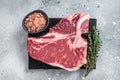 Raw dry aged wagyu porterhouse beef steak, uncooked T-bone on marble board with thyme. Gray background. Top view Royalty Free Stock Photo