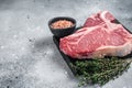 Raw dry aged wagyu porterhouse beef steak, uncooked T-bone on marble board with thyme. Gray background. Top view. Copy Royalty Free Stock Photo