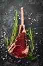 Raw dry steak on bone. Tomahawk steak on a black stone background. Top view. Royalty Free Stock Photo