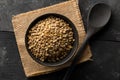 Raw, dry, uncooked brown lentil legumes in black bowl on wood table background top view flat lay from above